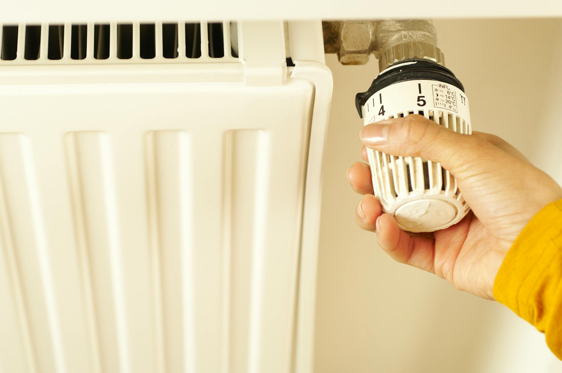 Dłoń regulująca termostat grzejnika w domowej instalacji grzewczej