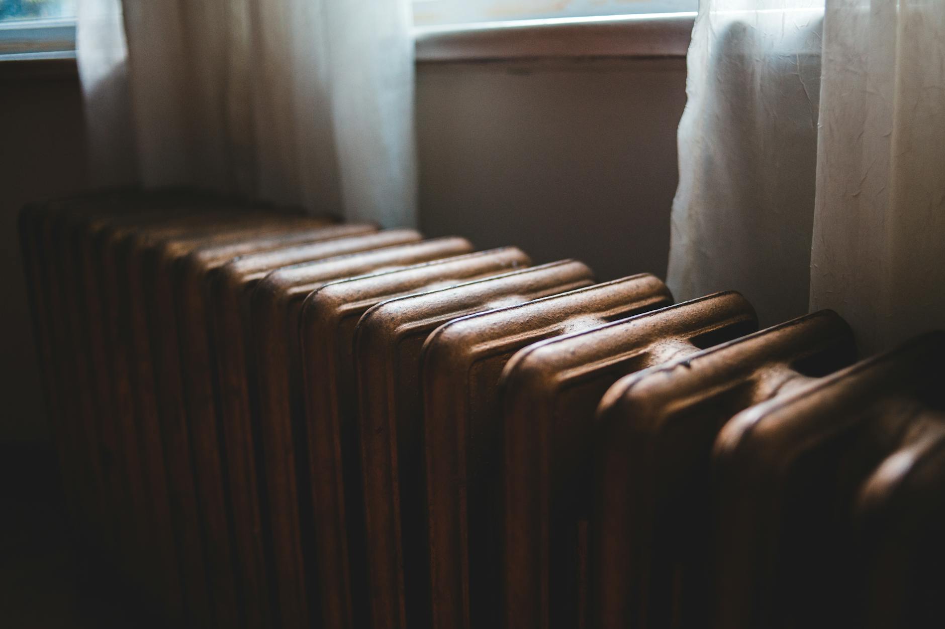 Stary żeliwny grzejnik pod parapetem z zasłoną w mieszkaniu
