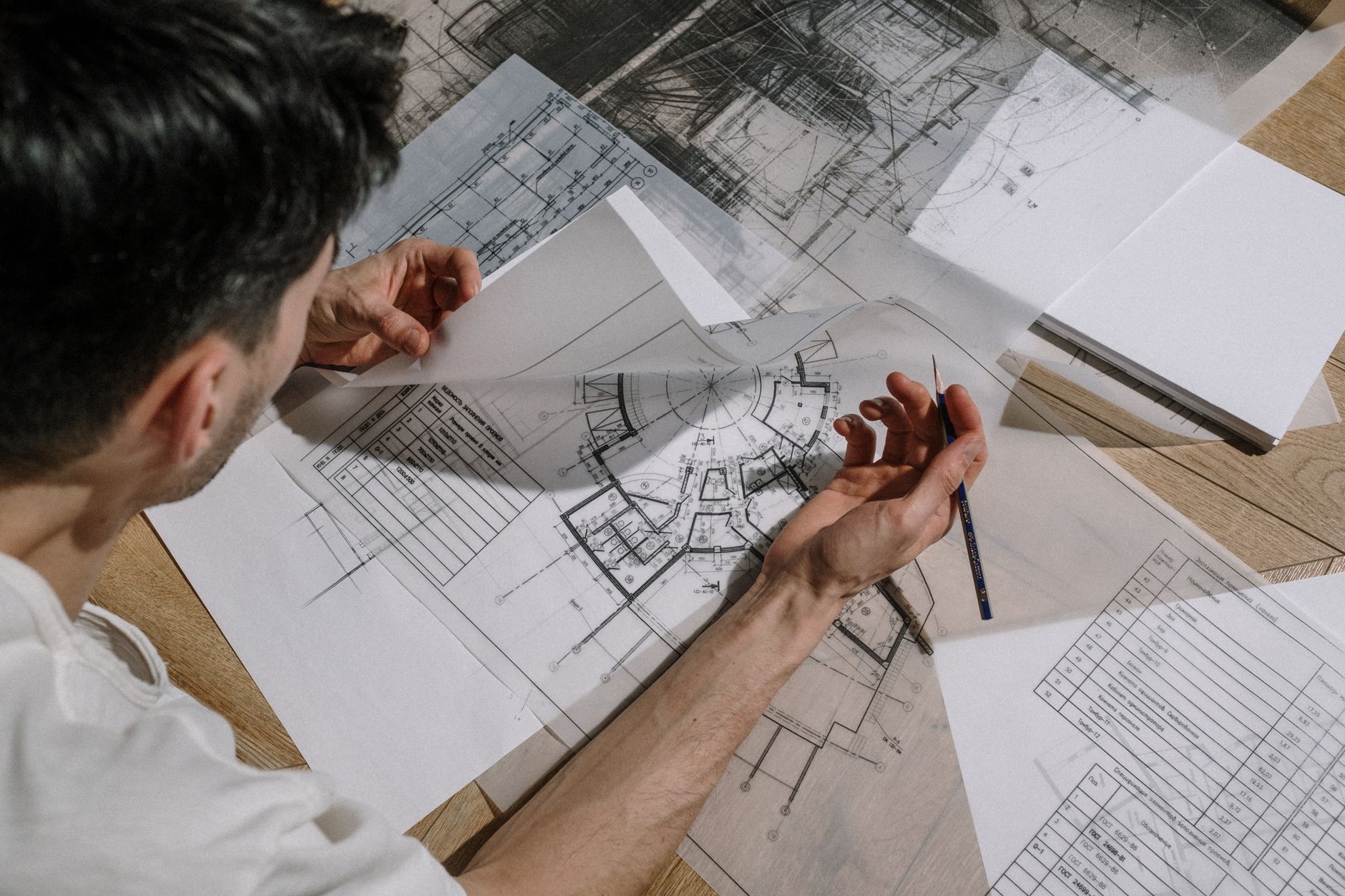 Architekt pochylony nad stołem analizuje i szkicuje rysunki wykonawcze
