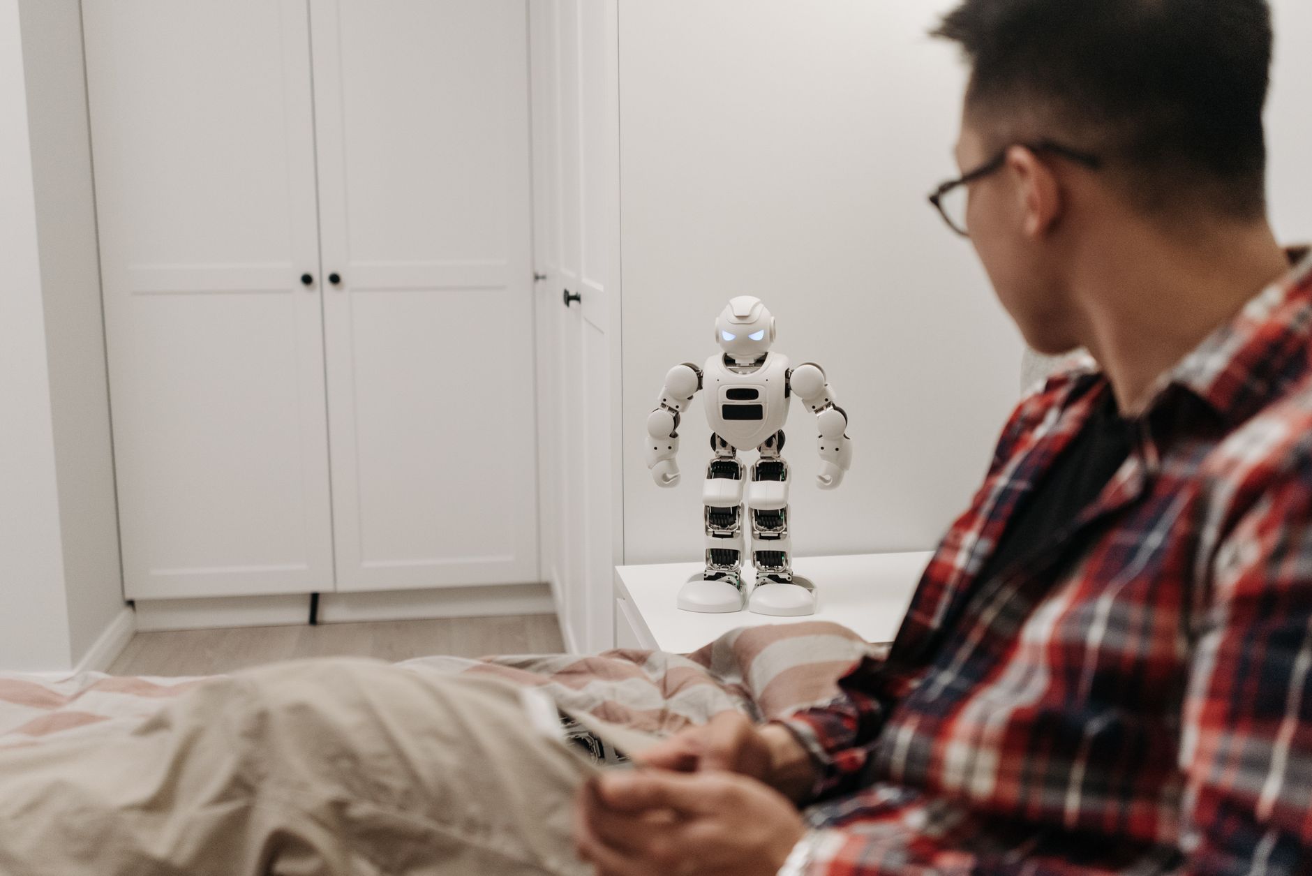 Mężczyzna bada małego robota na stole w nowoczesnej sypialni Mężczyzna bada małego robota na stole w nowoczesnej sypialni